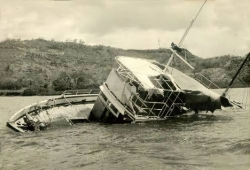 Photograph of the MV Joyita listing severely to port, being towed by another vessel.